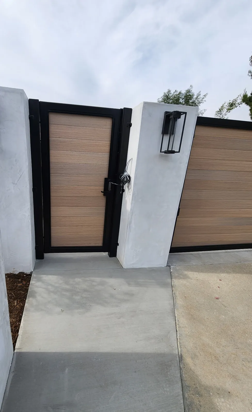 Wood-look pedestrian gate between stucco pillars with lantern lights
